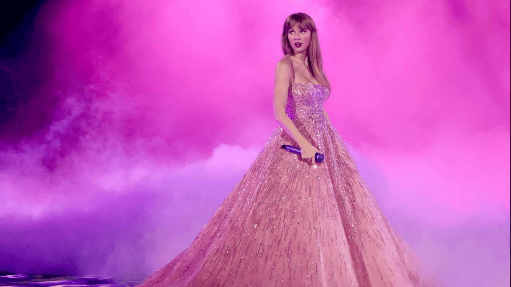 Taylor Swift performing on stage in a sparkling pink gown with purple lights and smoke background.