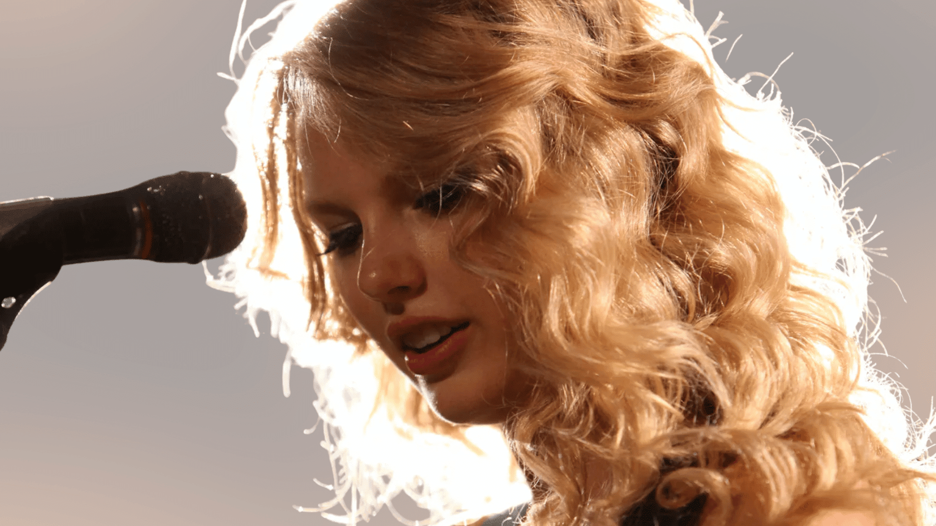 Taylor Swift with long curly hair, looking over her shoulder in a dark studio portrait