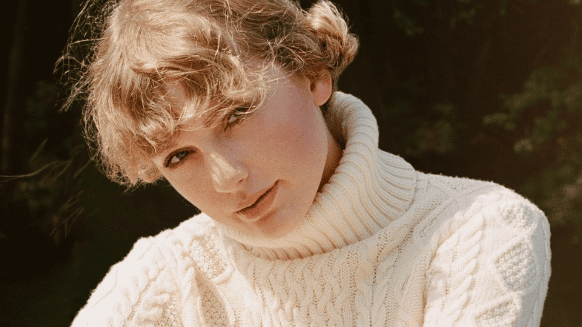 Taylor Swift in a cream cable-knit sweater outdoors with wind-blown hair