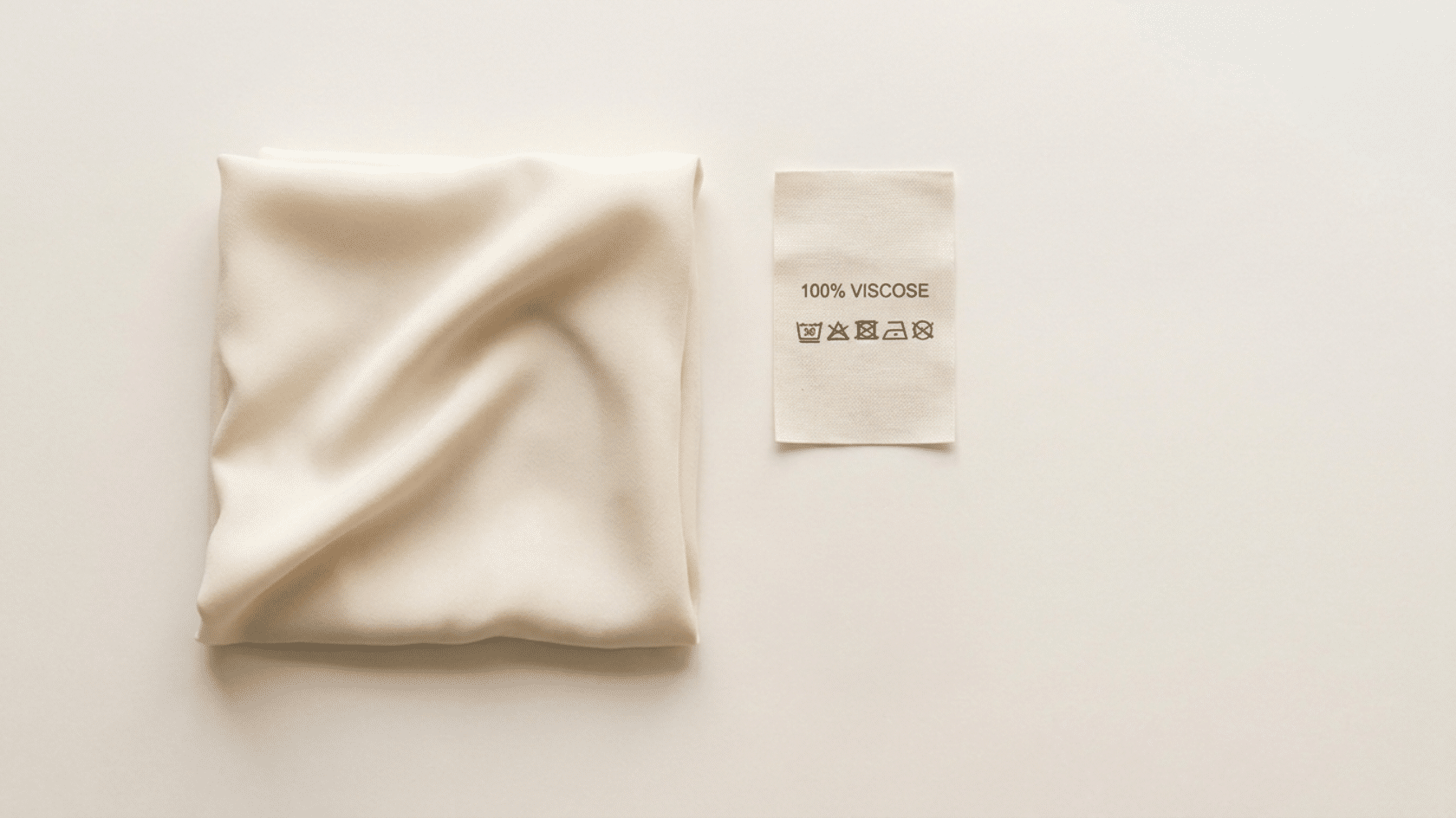 Flat lay showing what is viscose fabric: a plain fabric swatch, and a viscose clothing label on a neutral background.