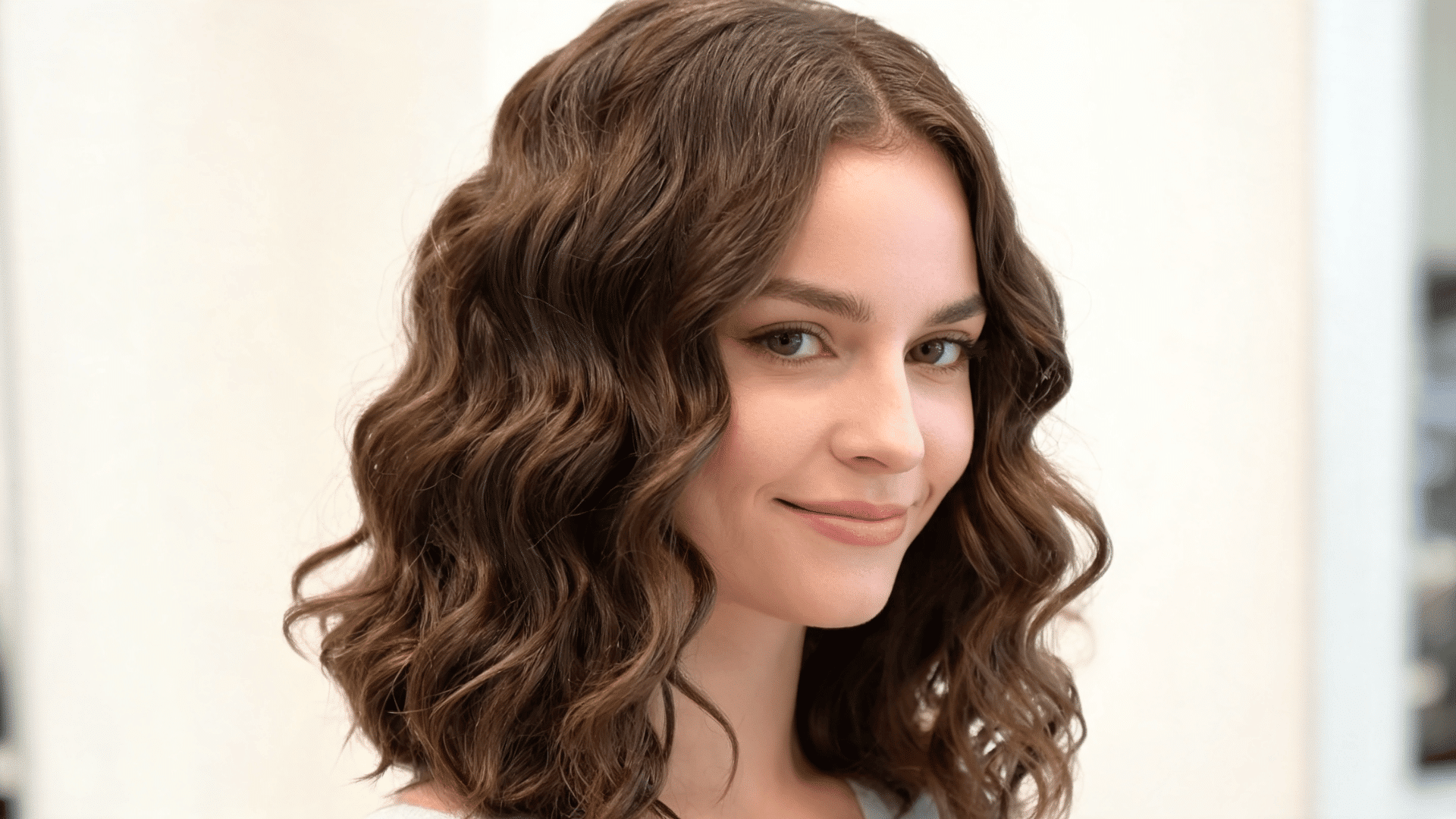 Woman with a mid-length natural curl sew-in hairstyle featuring soft curls and face-framing volume.