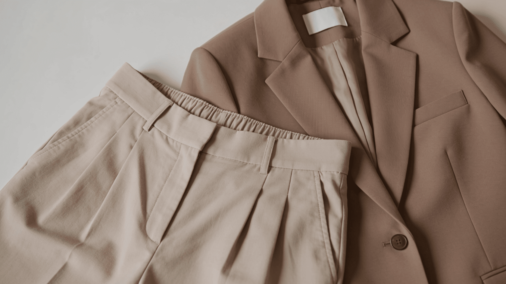 Tight waistband pants and structured blazer laid flat on a neutral background