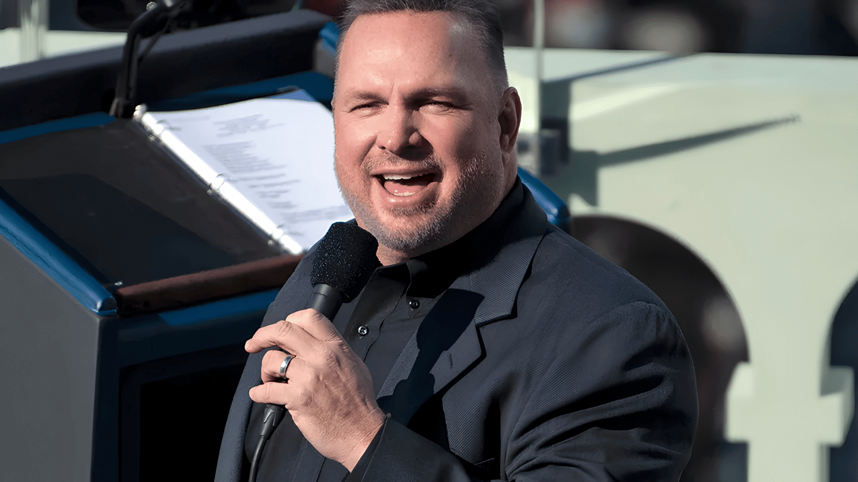 Garth Brooks singing into a microphone outdoors during a live event.