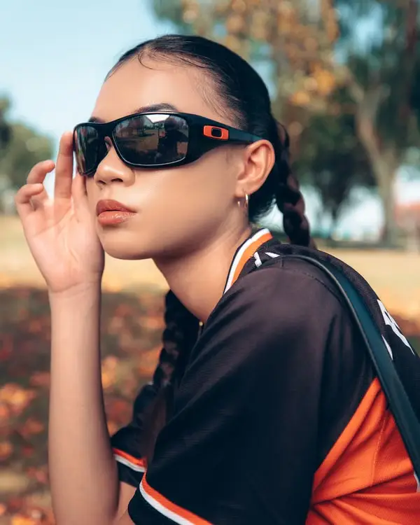 Person wearing black sunglasses and sports jersey in sunny outdoor park setting