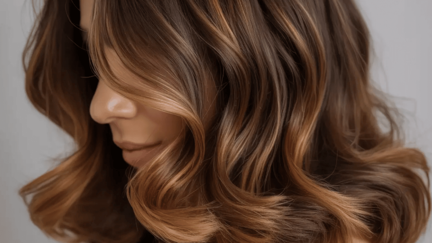 Brown hair with caramel highlights framing the face and waves throughout the hair.