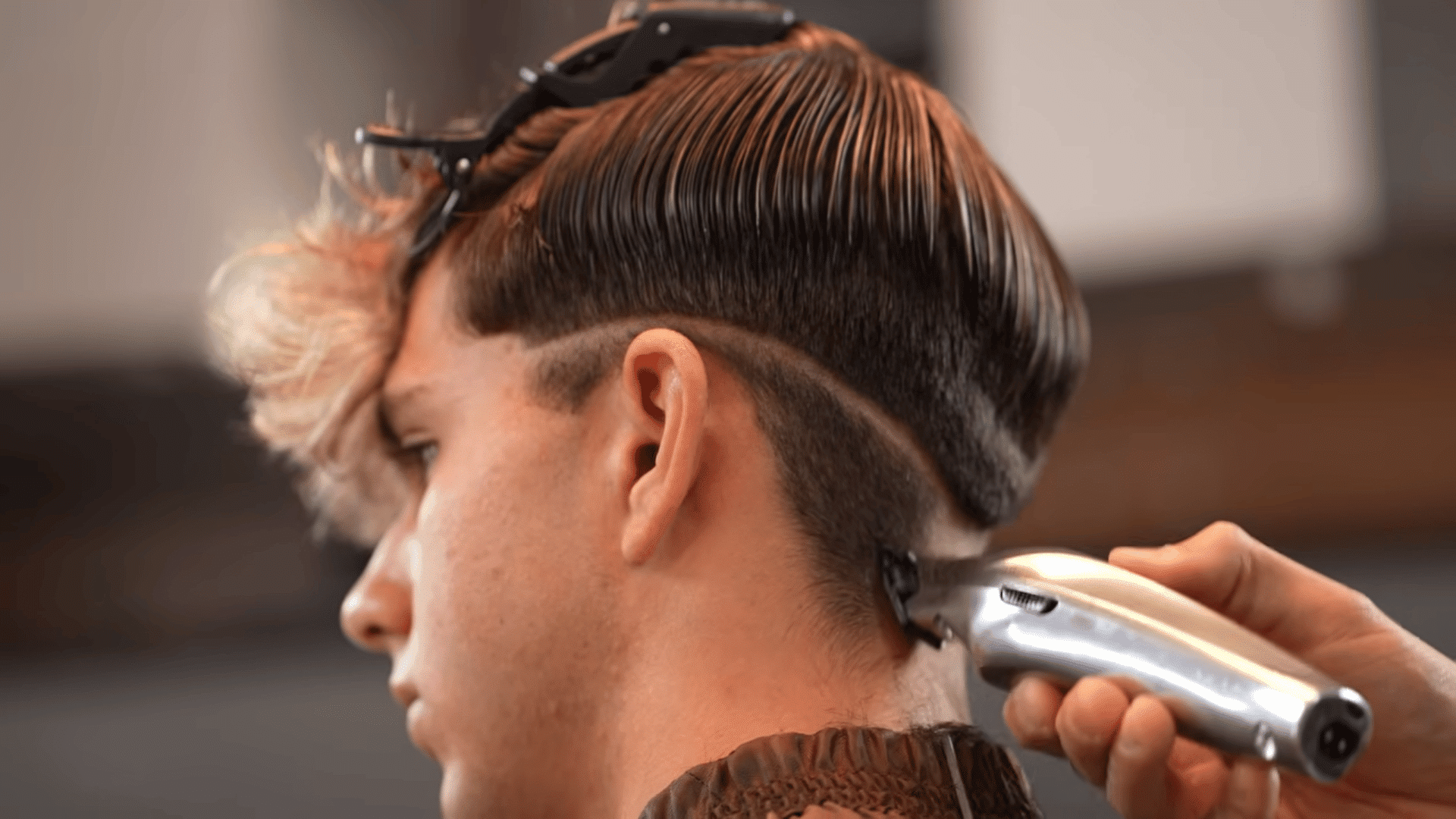 A barber using electric clippers to create a fade and guideline on a client's dark hair.
