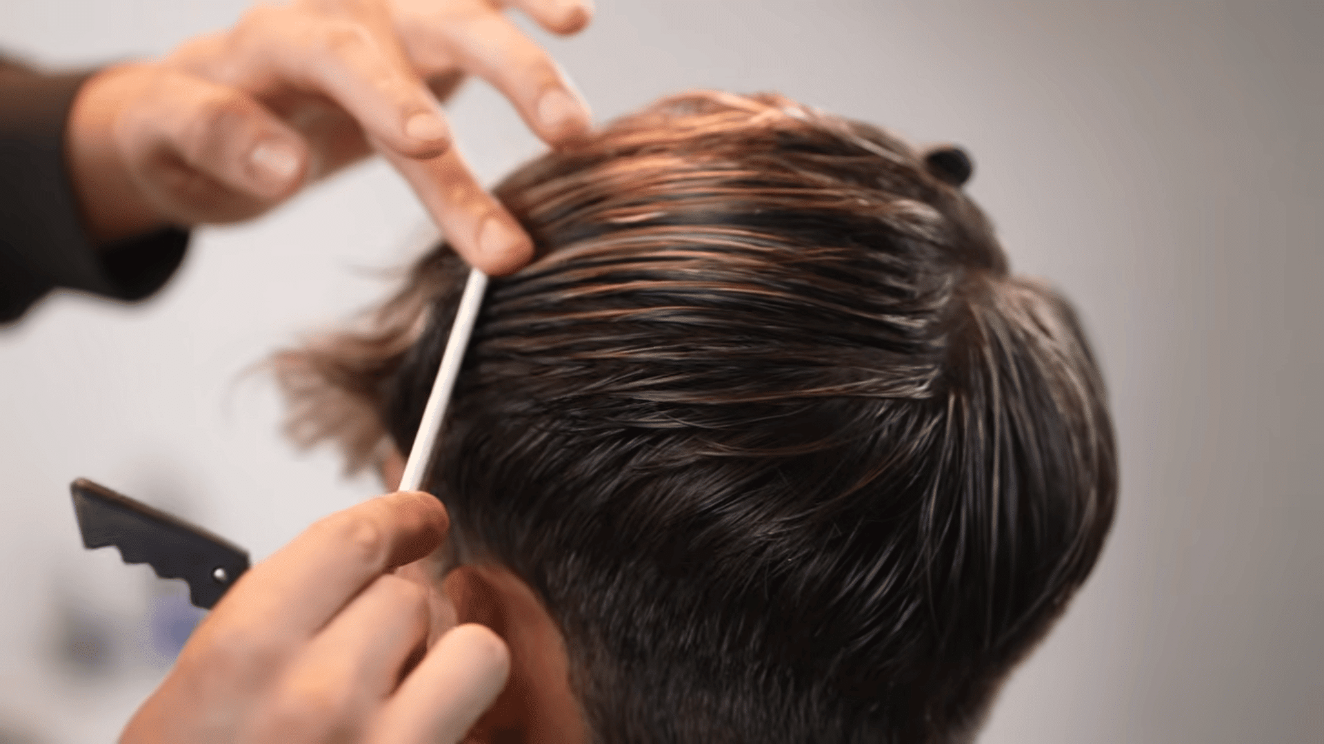 A barber's hands using a white comb to section a client's damp, dark brown hair.