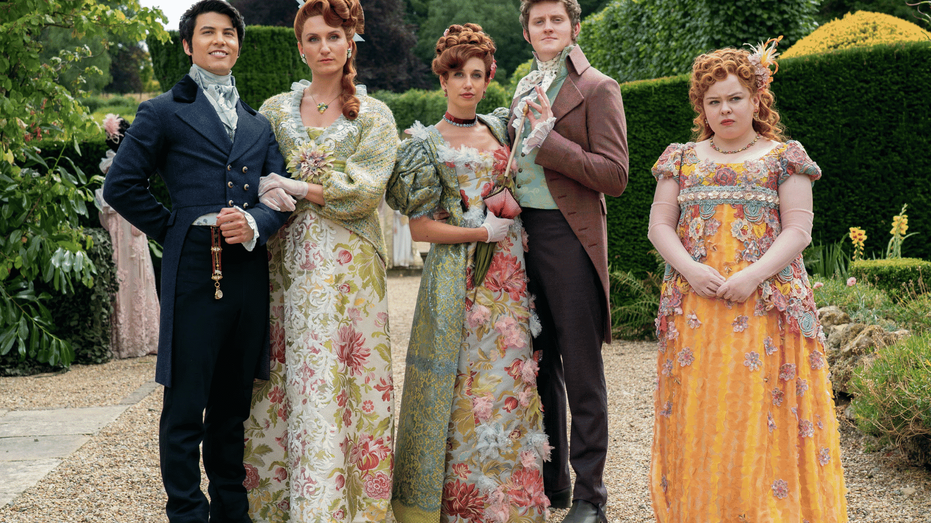Bridgerton cast in a garden wearing ornate Regency era costumes with floral gowns, tailored coats, and period accessories.