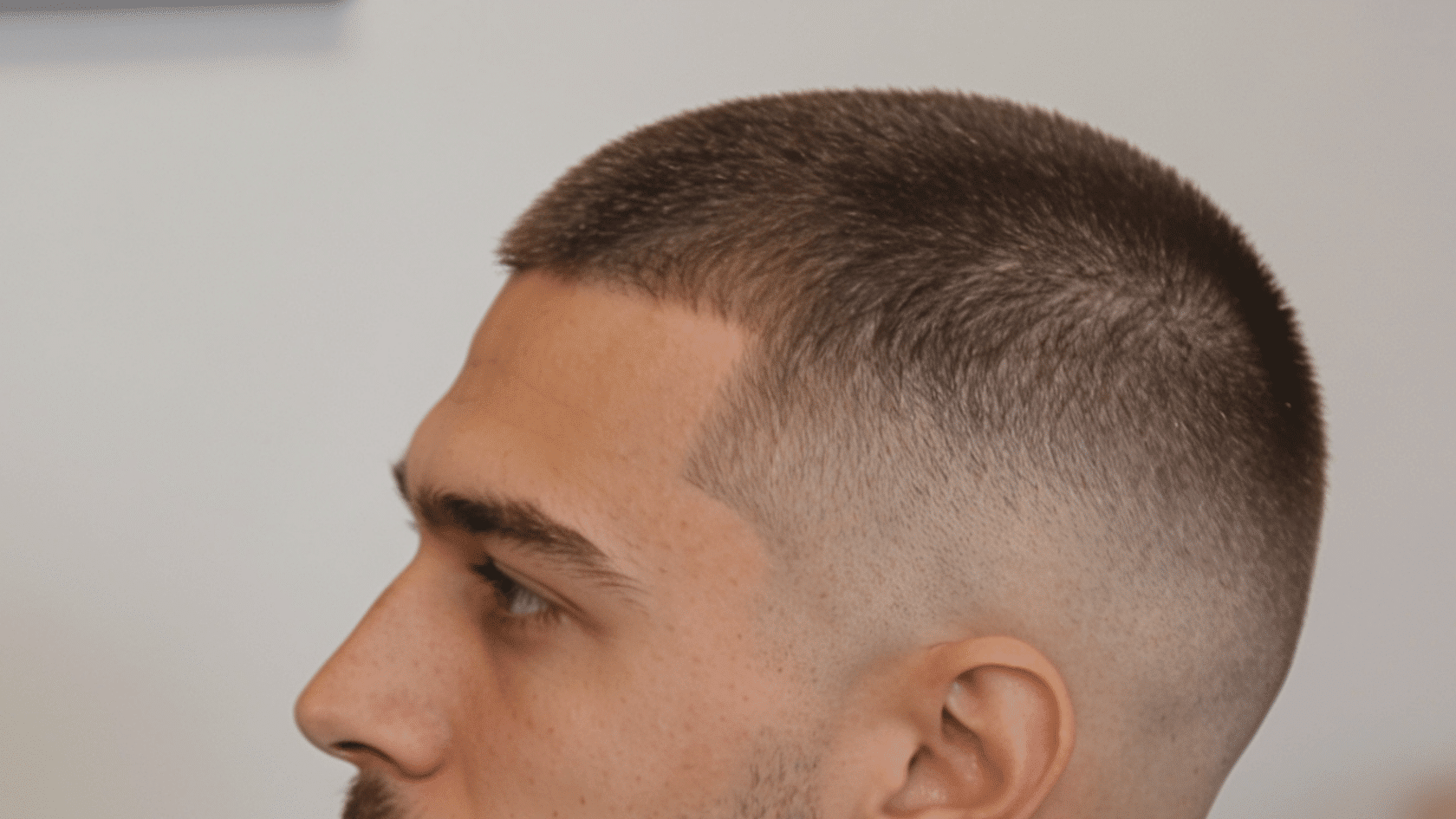 Buzz cut with a subtle side taper and a short, neatly trimmed beard
