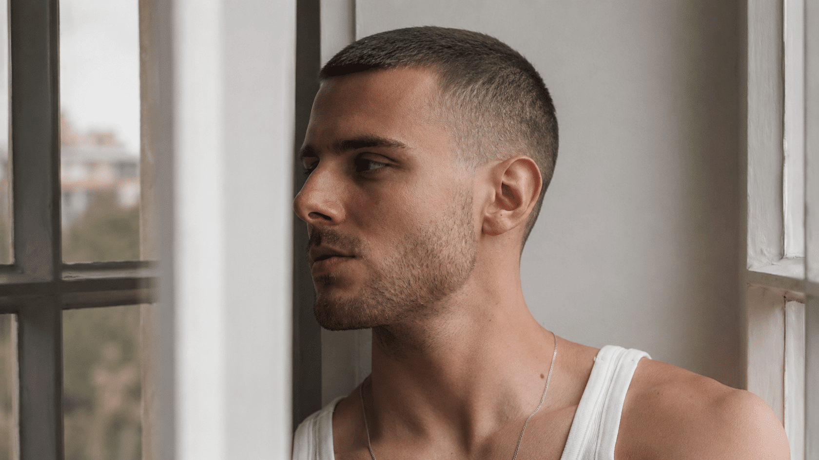 Man with a short buzz cut standing by a window in natural light.