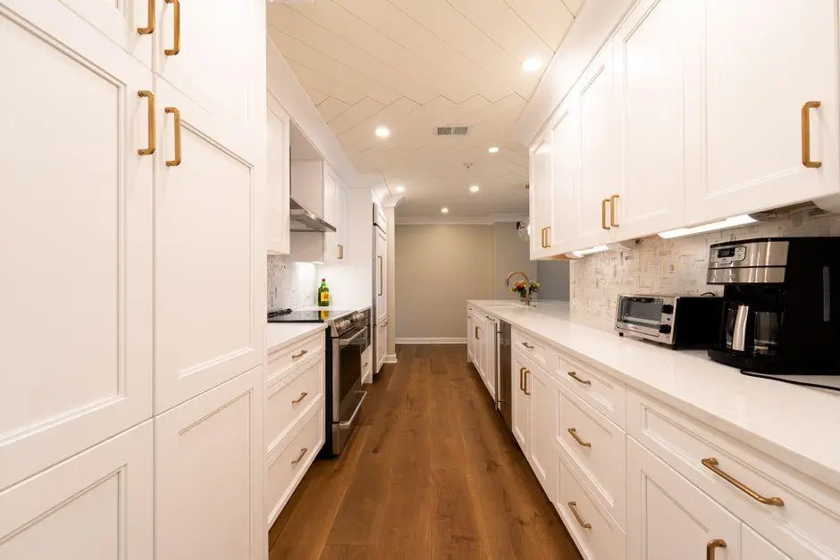 Modern kitchen with white cabinets, brass handles, stainless steel appliances, and wooden floor
