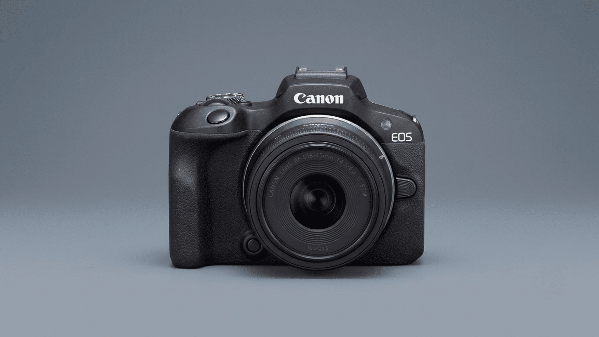 Canon EOS R100 mirrorless camera with attached lens displayed on a blue-gray background.