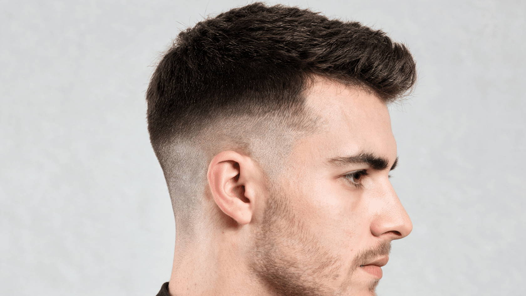 Man with a classic fade haircut and short textured top shown in side profile.