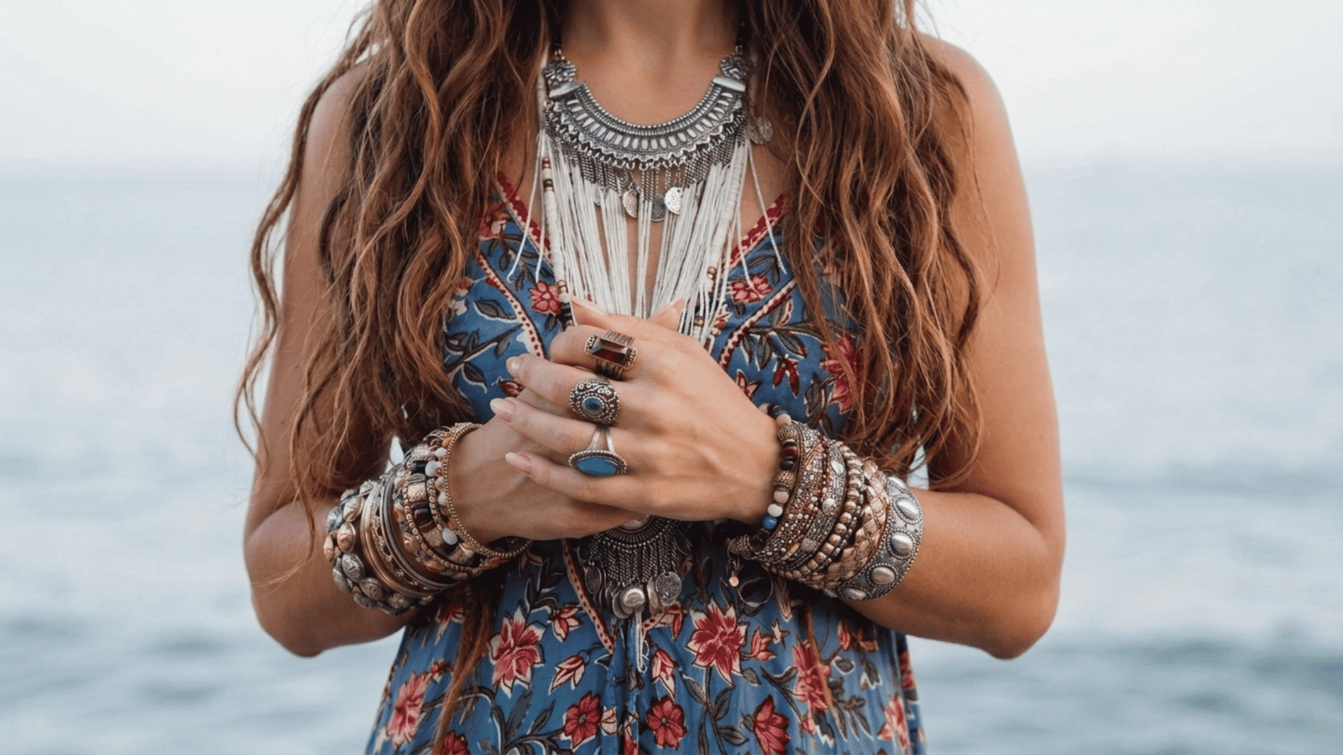 Close-up of a woman in a floral dress showing a boho look with layered statement necklaces, rings, and stacked bracelets