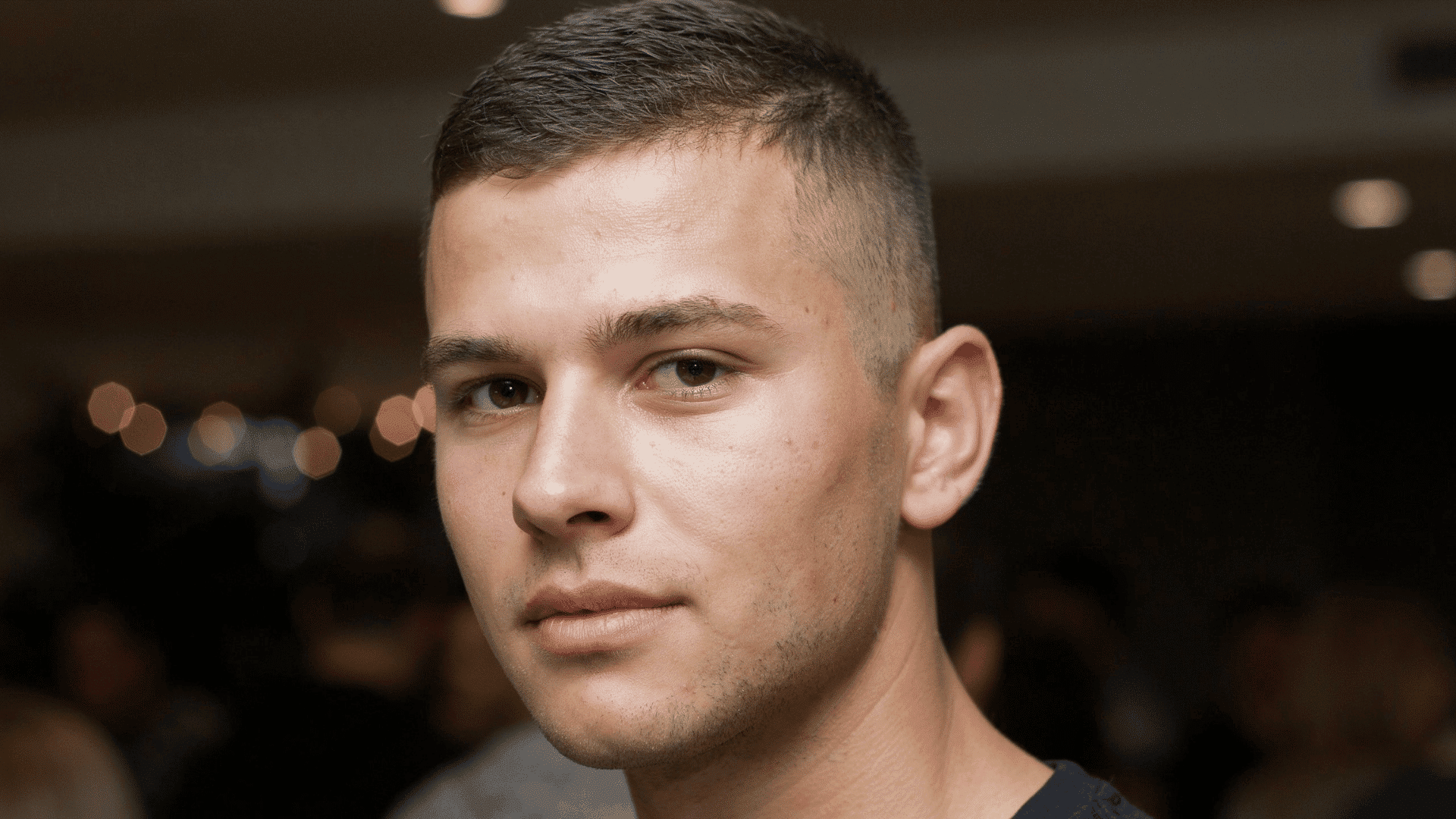 Close-up of man's face with short cropped haircut, fade on sides, brown eyes, indoor lighting with bokeh blurred background