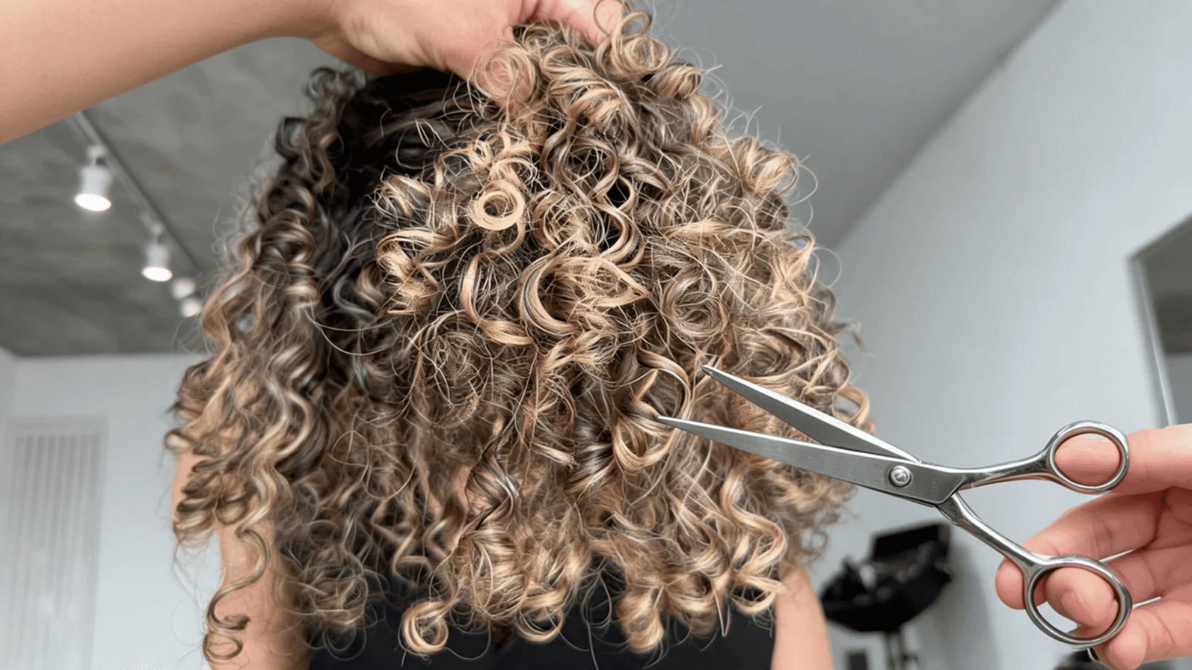 Coily hair viewed from the back with a comb and scissors near the ends in a salon setting