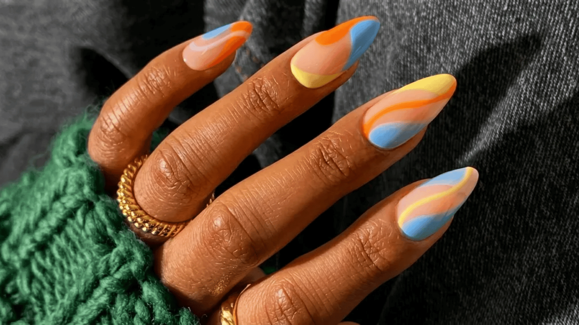 hand with multicolor abstract nail art on long nails, gold ring on finger, green knitted sleeve