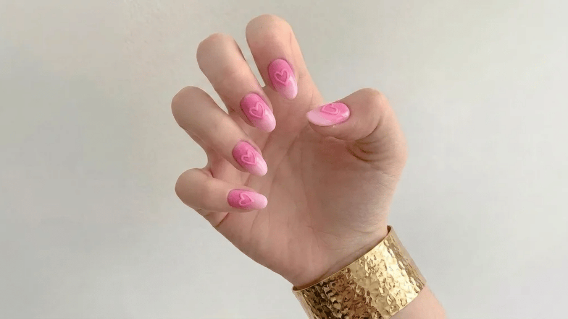 hand with pink nails featuring heart designs and gold bracelet on wrist