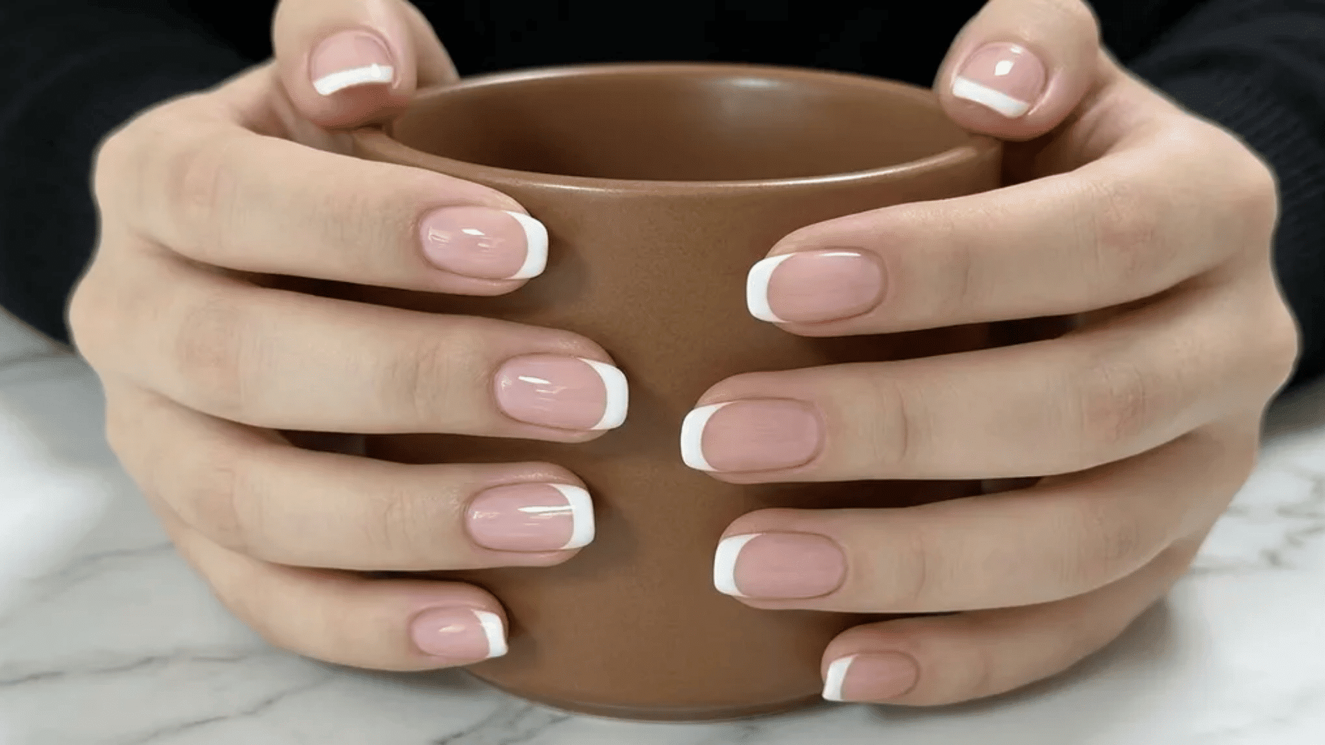 Hands holding a brown cup showing French manicure nails with pink base and white tips