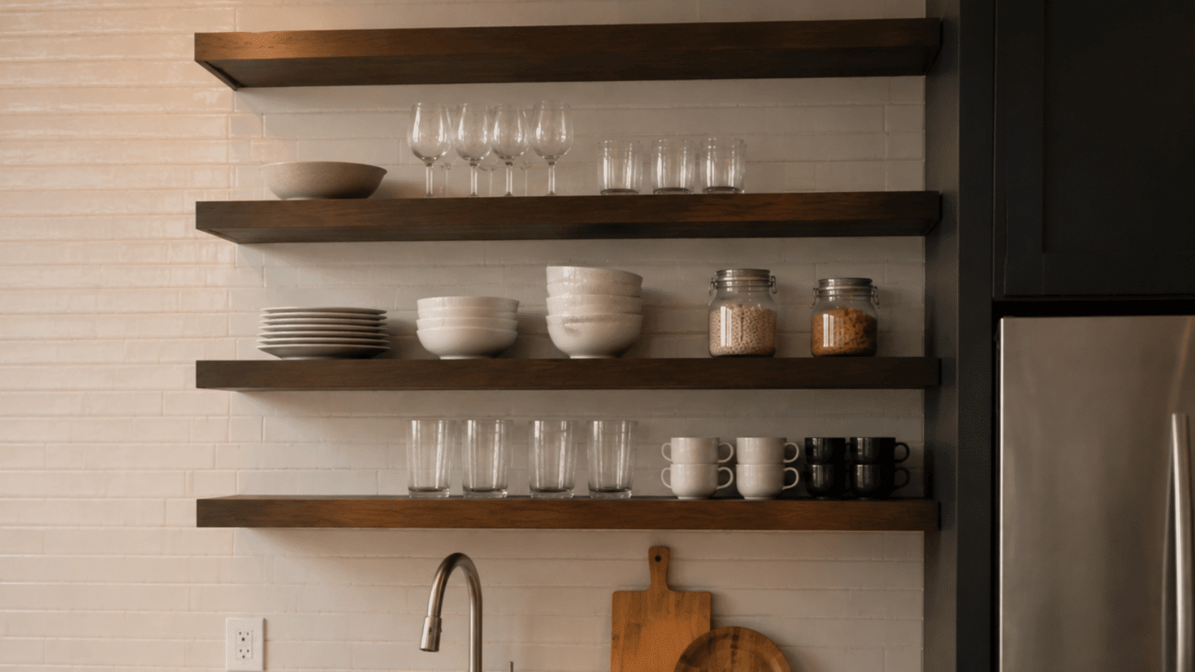 Kitchen wall with open wooden shelves holding plates, bowls, glasses, cups, and jars.