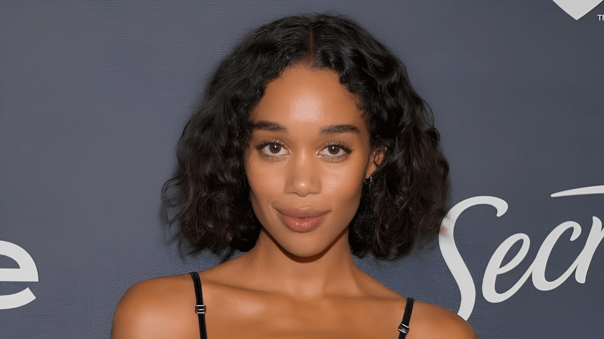 Laura Harrier with a curly bob haircut on a heart-shaped face.