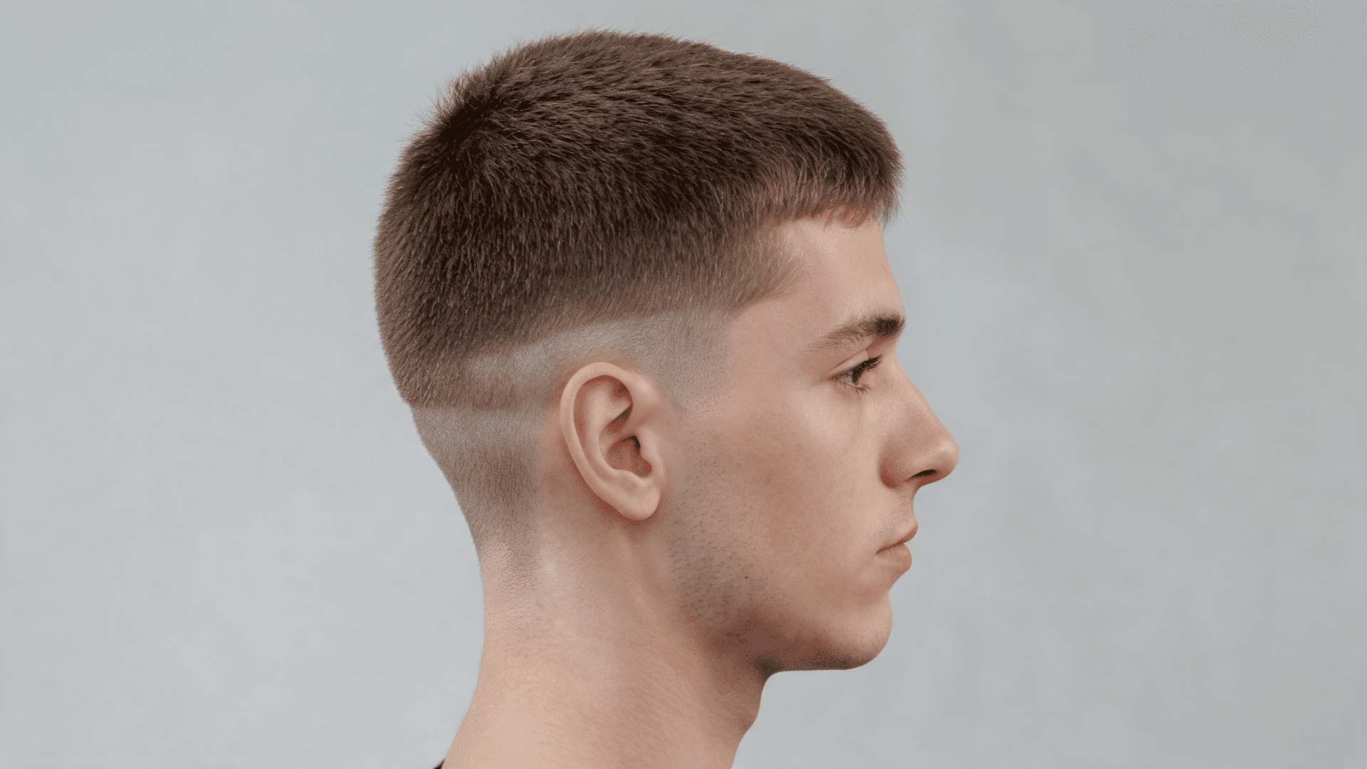 Man in profile, short cropped haircut, skin fade on sides and blurred light gray background
