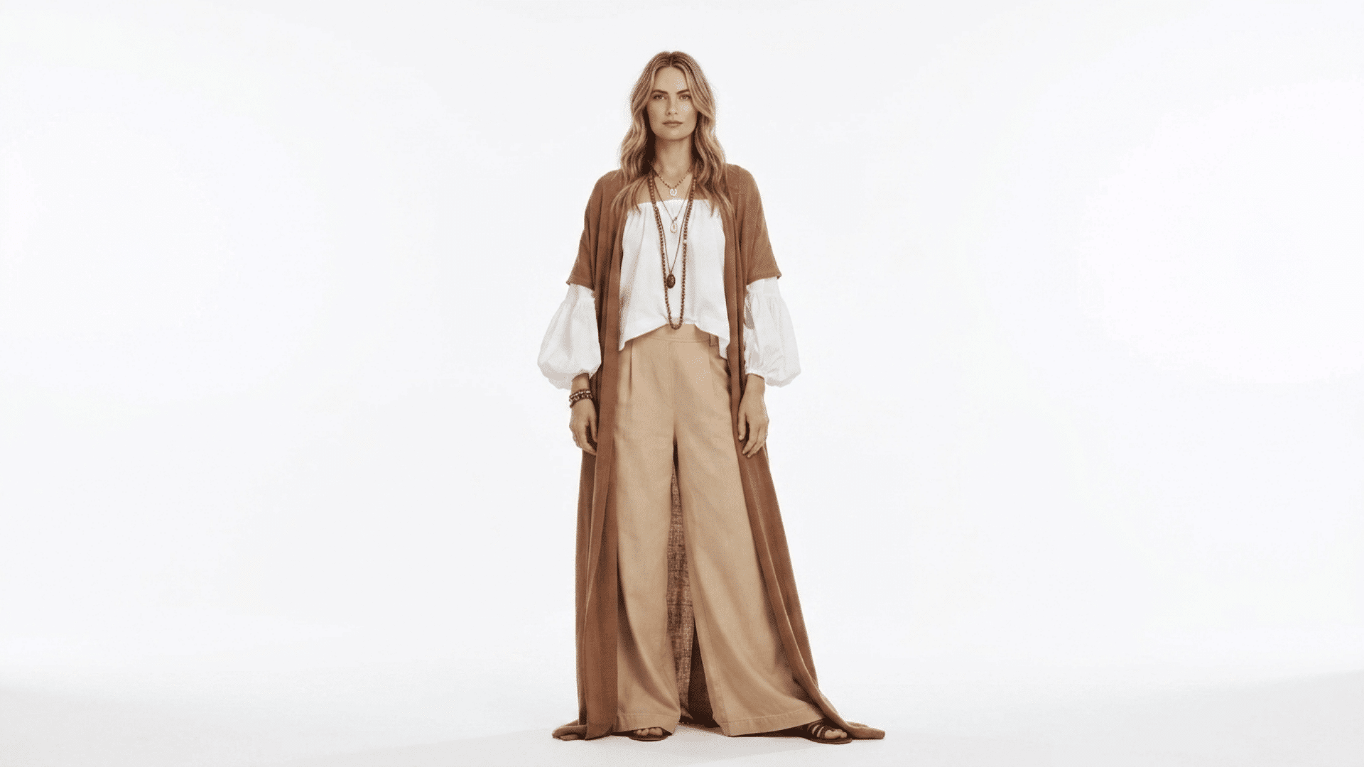 Model wearing a white peasant blouse, beige wide pants, and a long brown duster cardigan in a boho style look