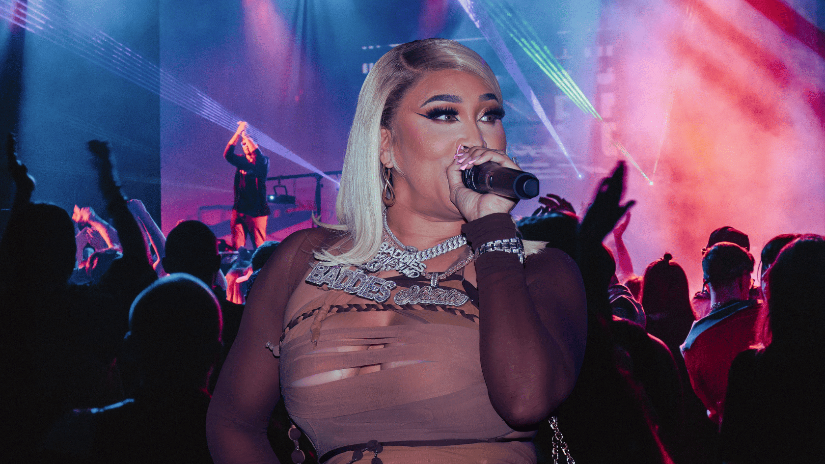 Natalie Nunn performing on stage with a microphone in front of a colorful concert crowd and lighting effects.