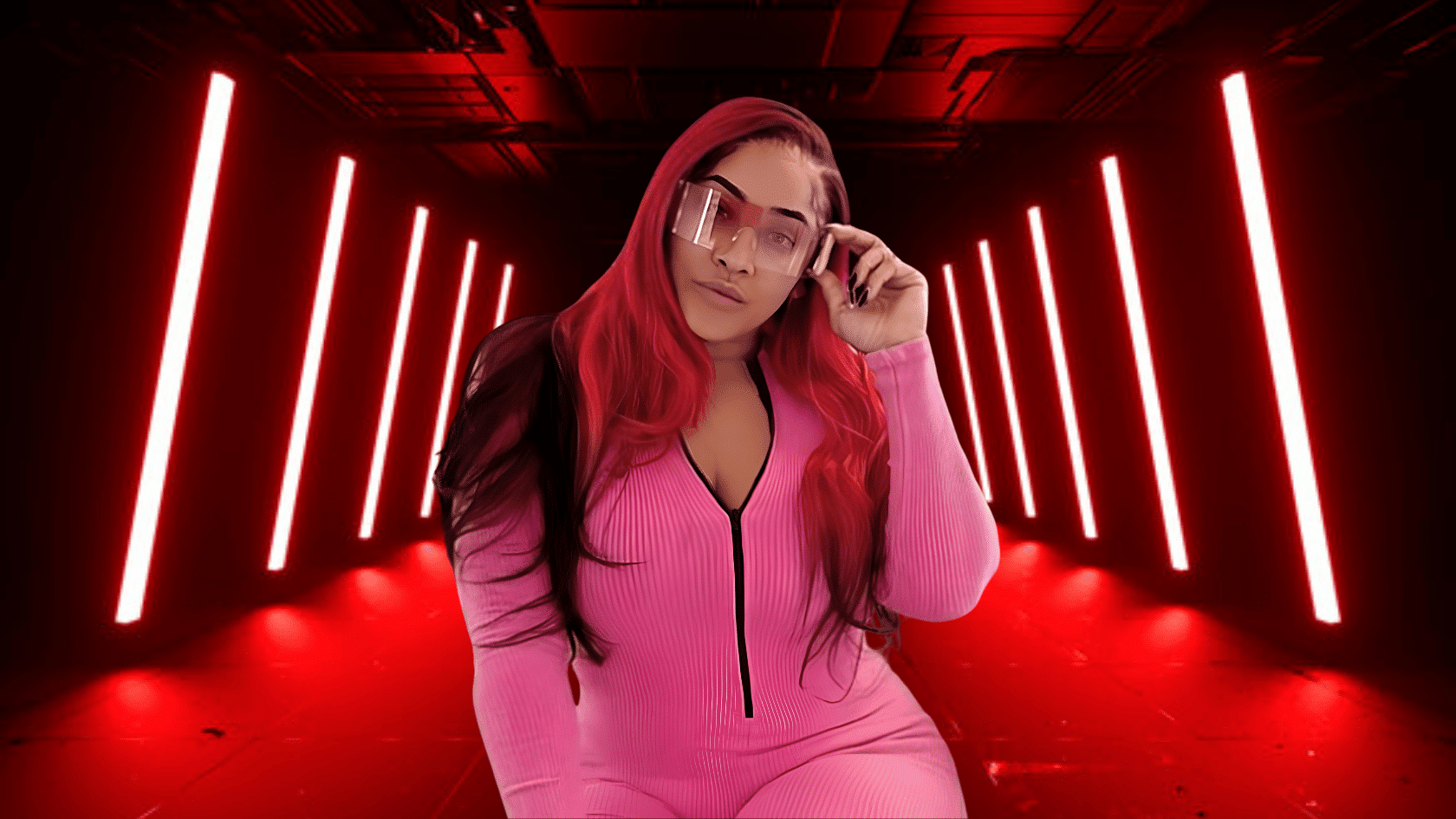 Natalie Nunn with red hair wearing pink outfit and sunglasses posing in a red neon light studio.