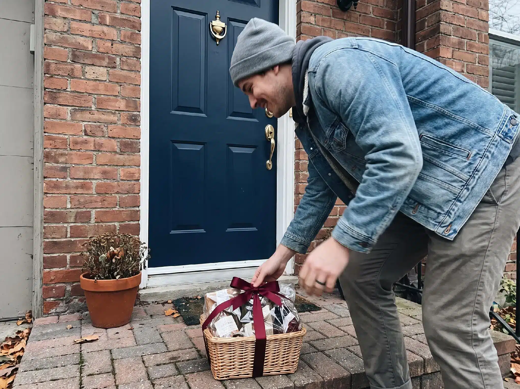 Man placing gift basket with red ribbon on brick doorstep in casual clothing