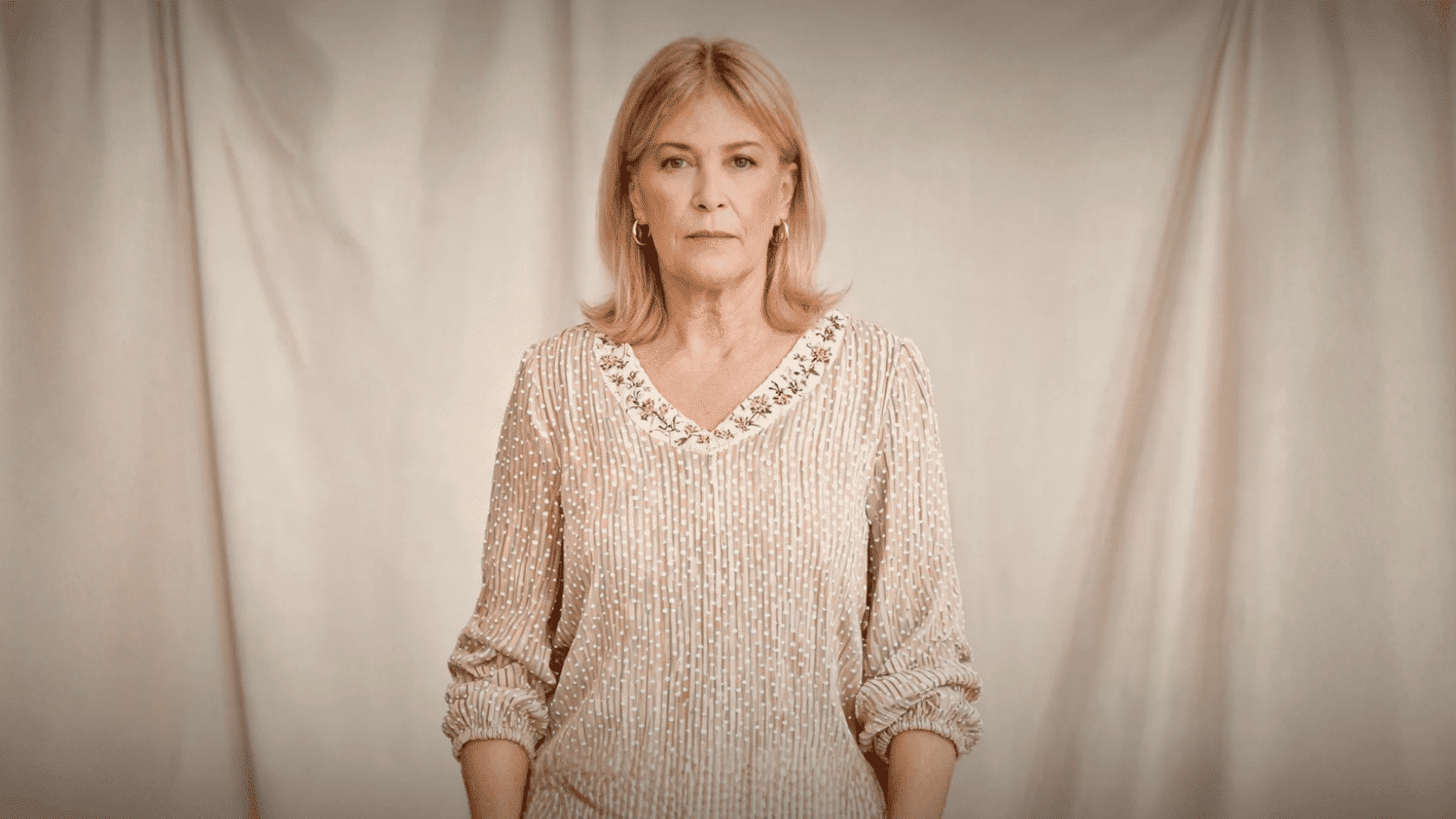 Older woman wearing a beige embroidered boho blouse against a neutral backdrop