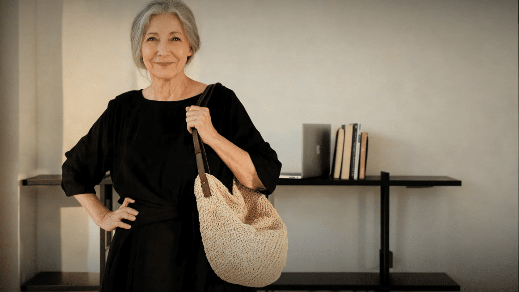 Older woman wearing a black boho dress with a woven shoulder bag indoors