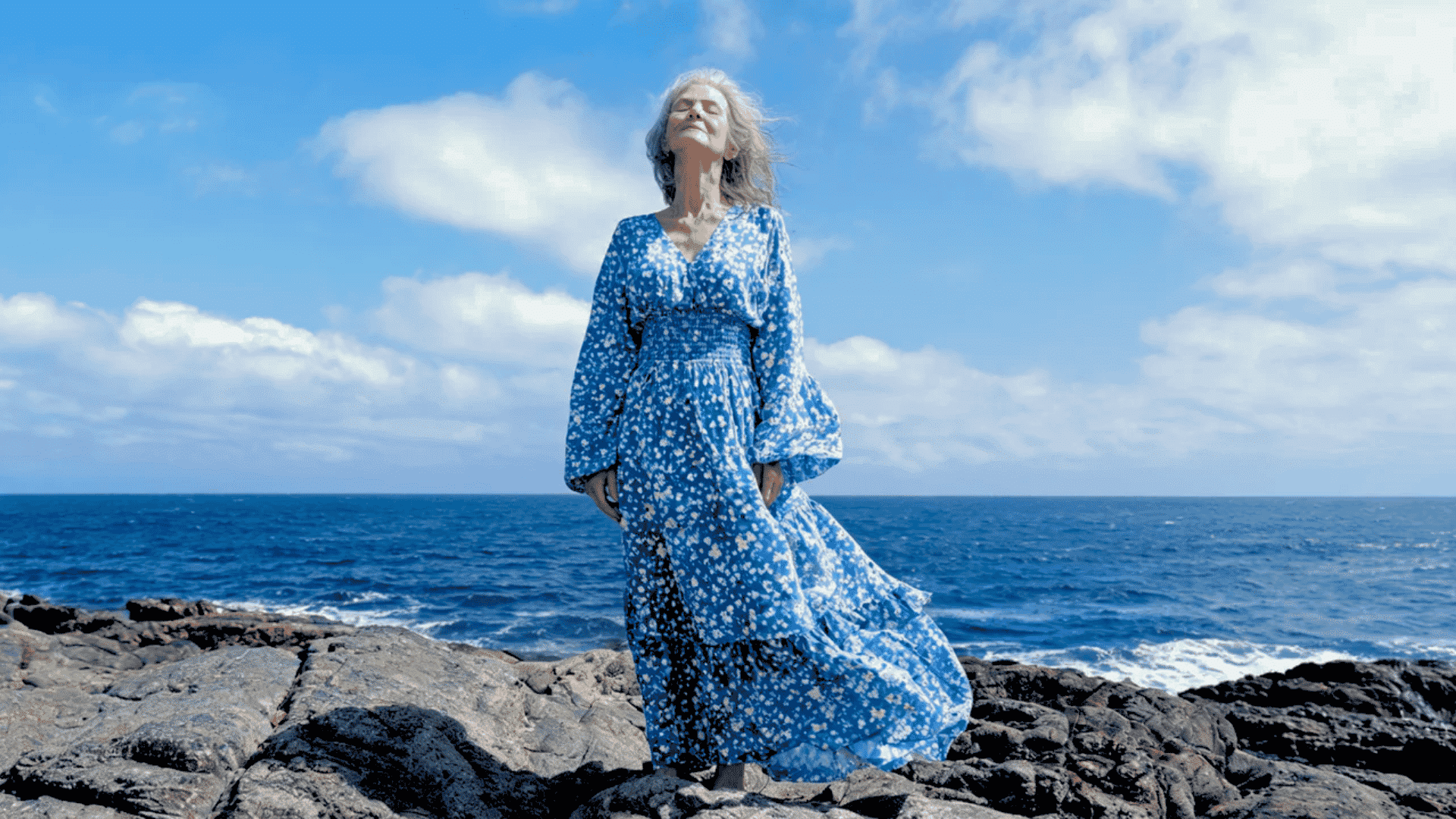 Older woman wearing a blue floral boho maxi dress by the ocean