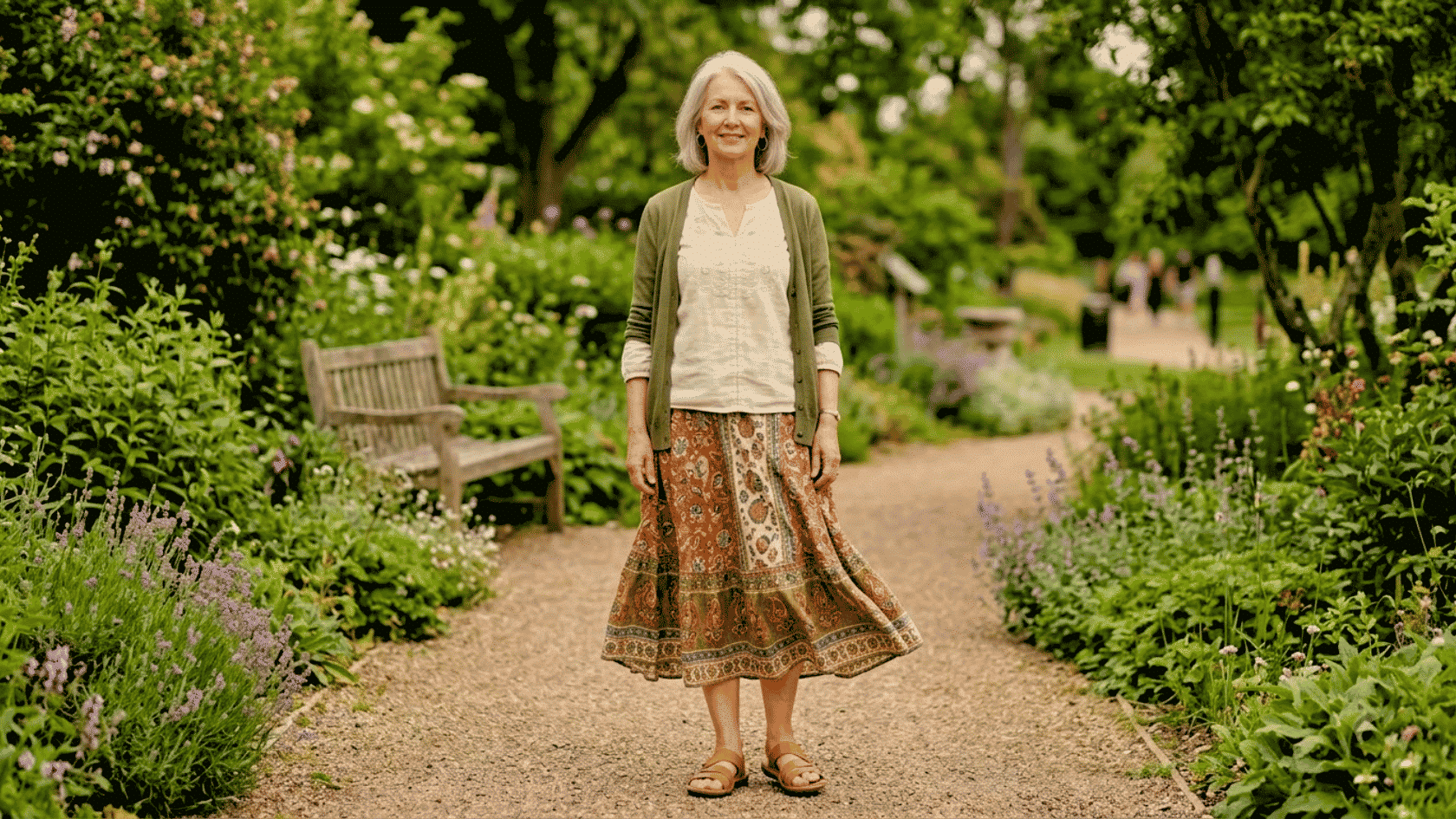 Older woman wearing a boho skirt and cardigan walking in a garden