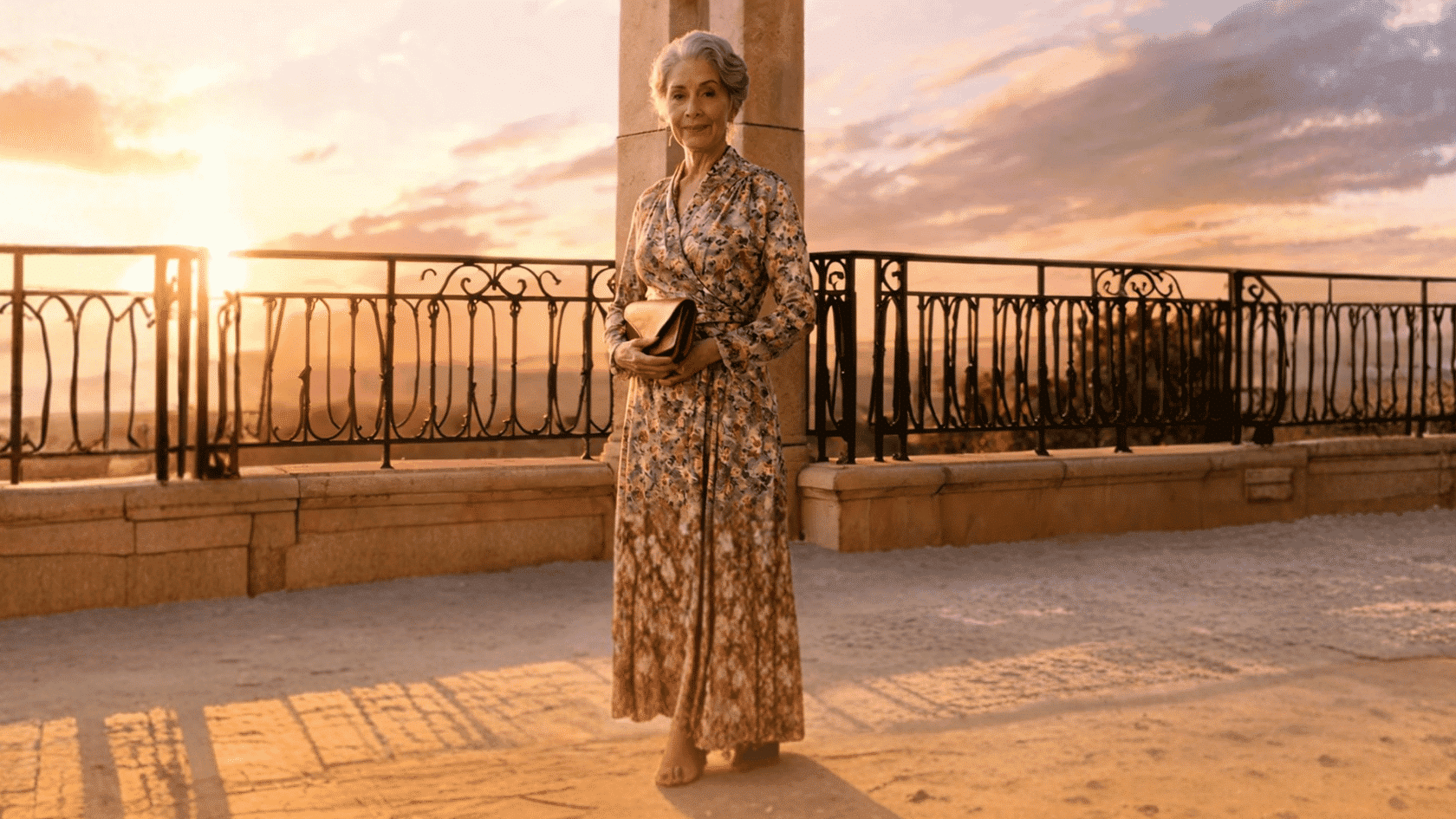 Older woman wearing a floral boho maxi dress at a sunset terrace.