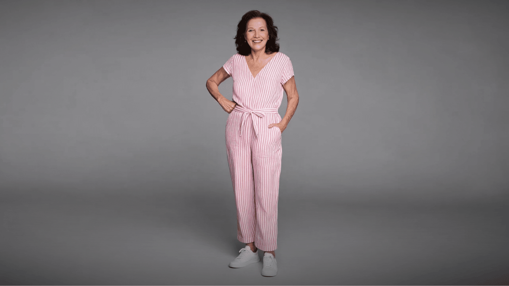 Older woman wearing a pink striped boho jumpsuit with white sneakers