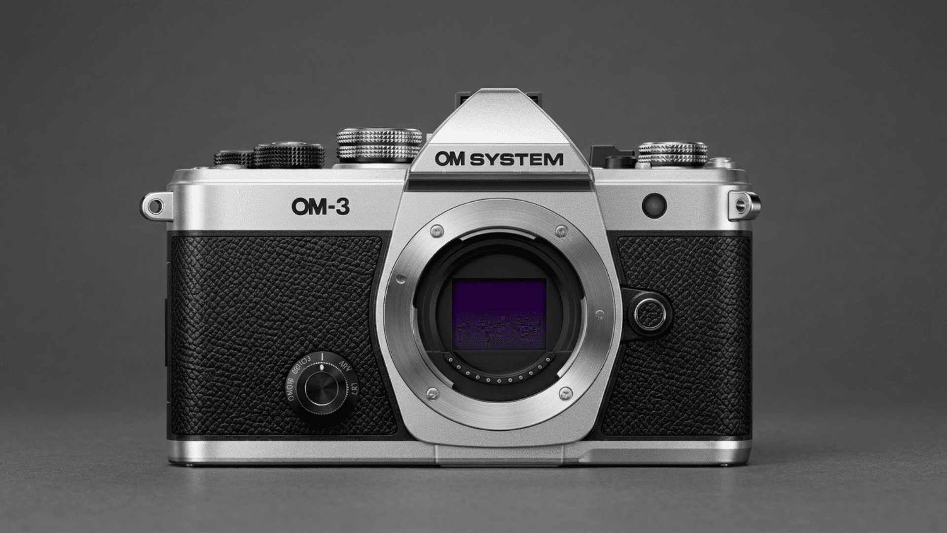 OM System OM-3 mirrorless camera body with exposed sensor on a dark gray background.