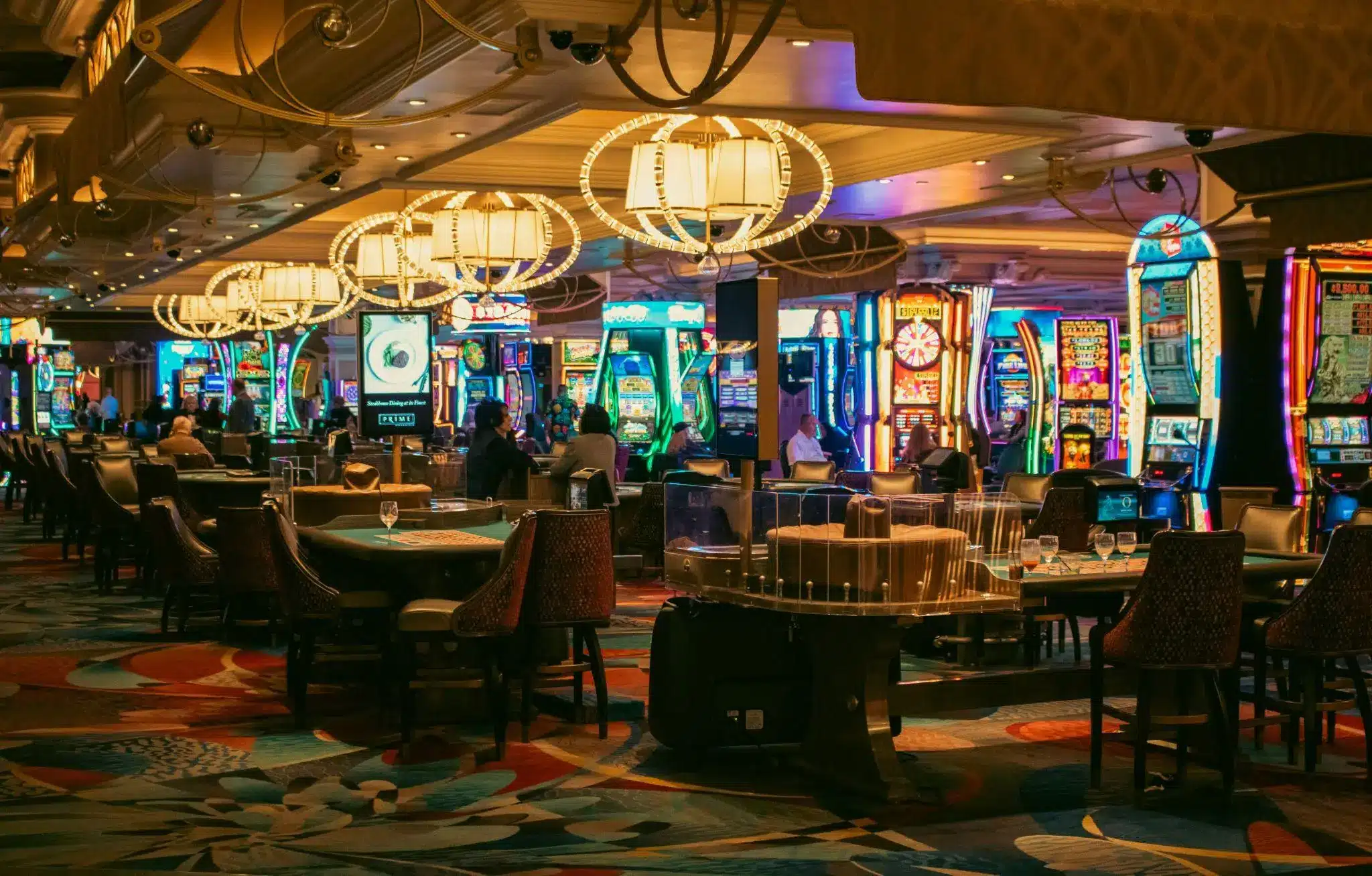 Casino interior with slot machines, gaming tables, and people under warm lighting