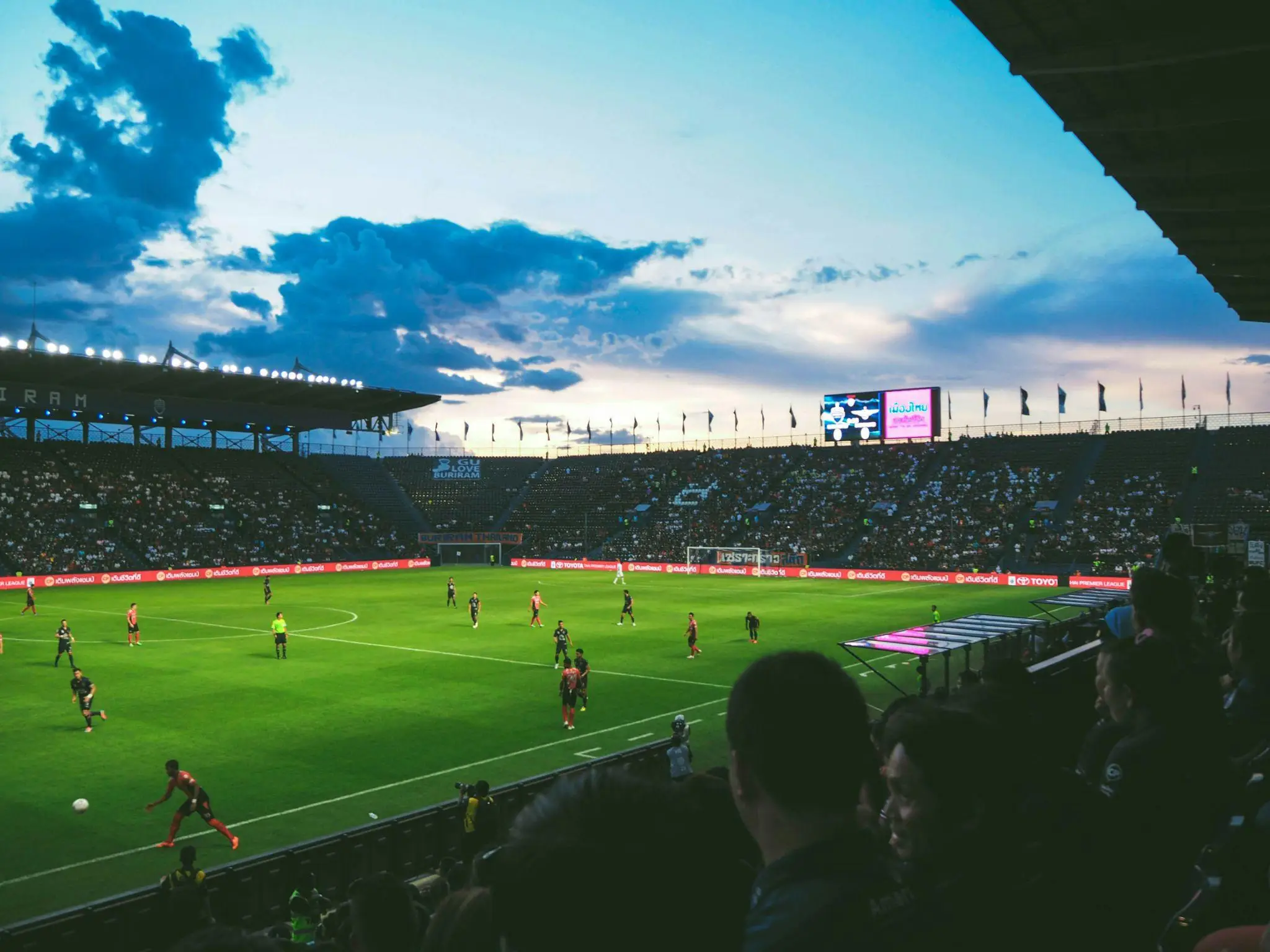 Football match taking place in a large stadium during sunset with a crowd watching
