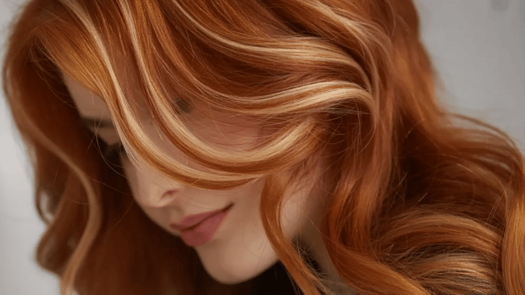 Copper hair with blonde highlights styled in loose waves covering part of the face.