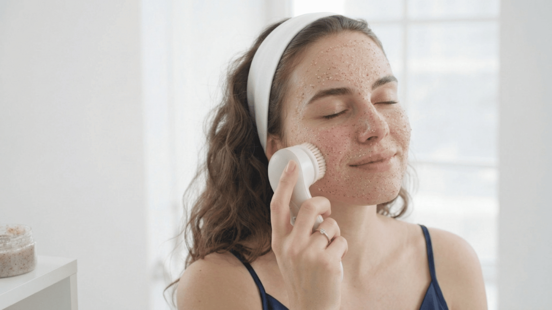 Person using a facial exfoliating brush to remove dead skin during skincare routine.