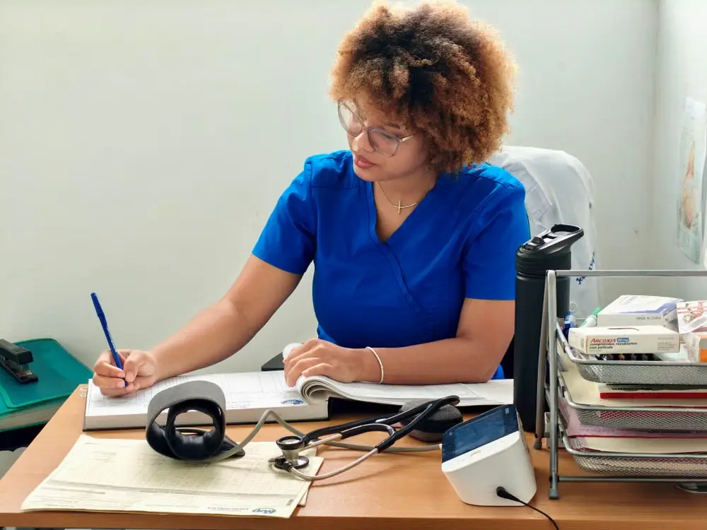 Healthcare professional writing in notebook at desk with stethoscope and medical supplies