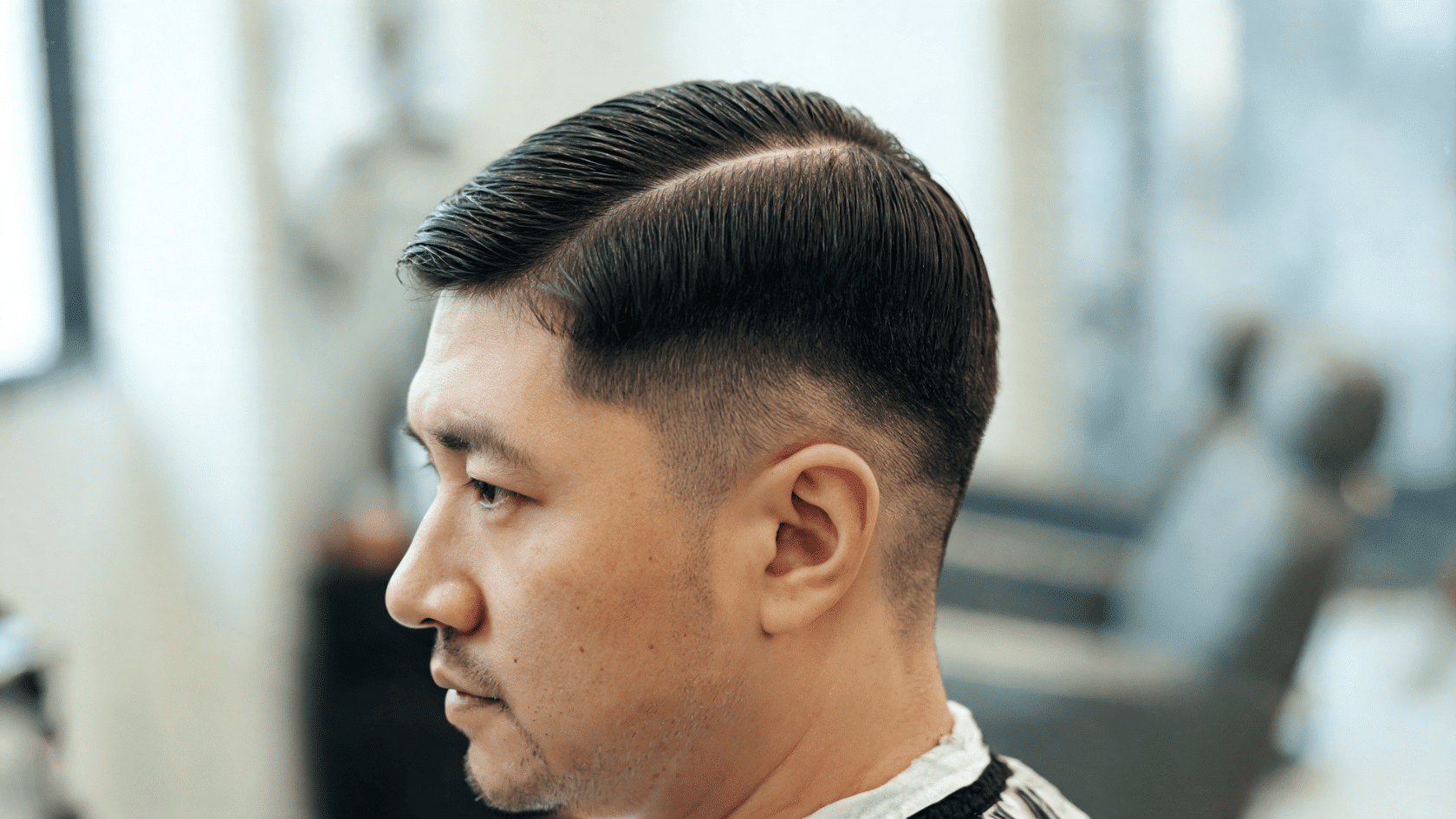 Man with a regular cut, side part, and neatly tapered sides in a barbershop.