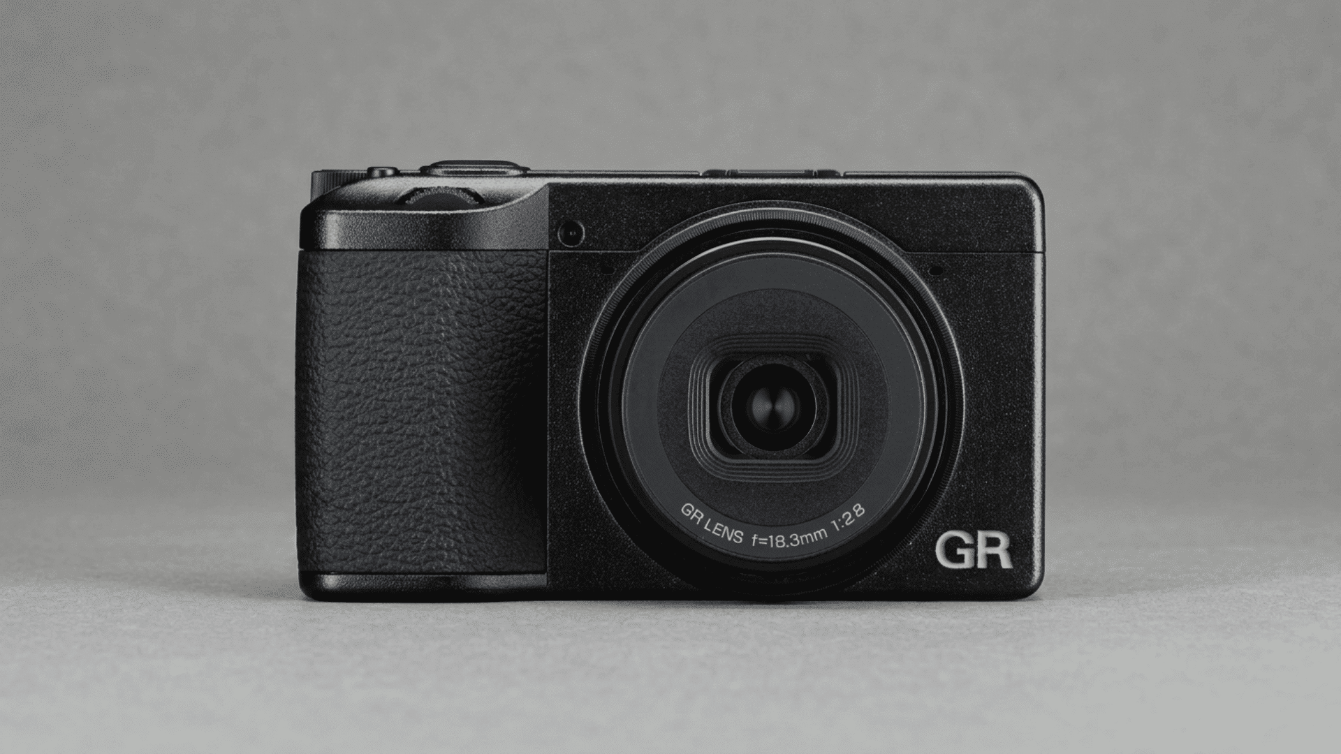 Ricoh GR IV compact camera with fixed lens displayed on a gray surface.