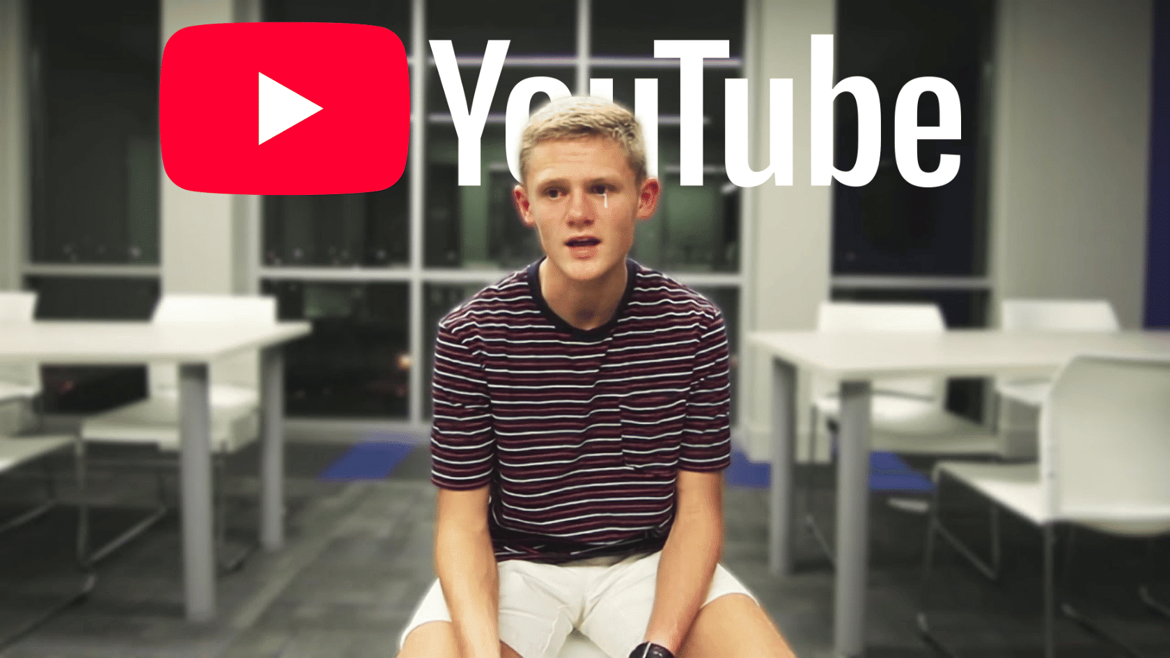 Ryan Trahan sitting indoors in a striped shirt with a large YouTube logo overlay in the background during a video recording.
