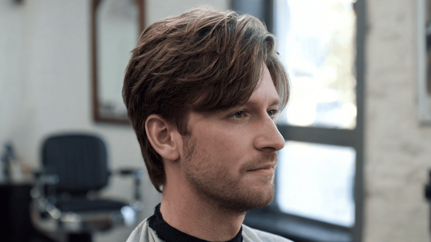 Man with a medium-length scissor cut haircut and soft layers styled in a natural flow, shown in a barbershop setting.