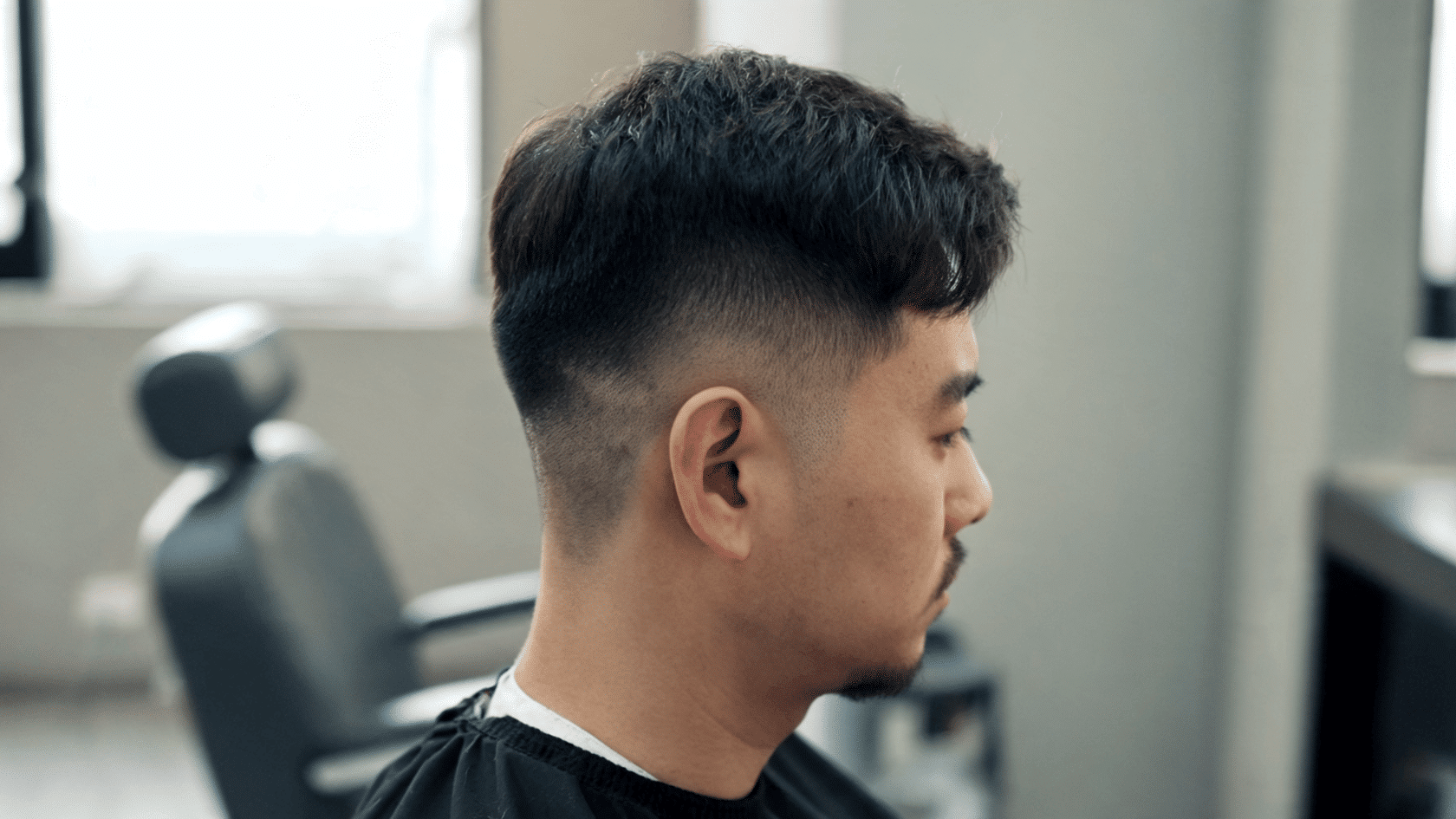 Man with a short back and sides haircut with a low fade, shown in side profile inside a barbershop.