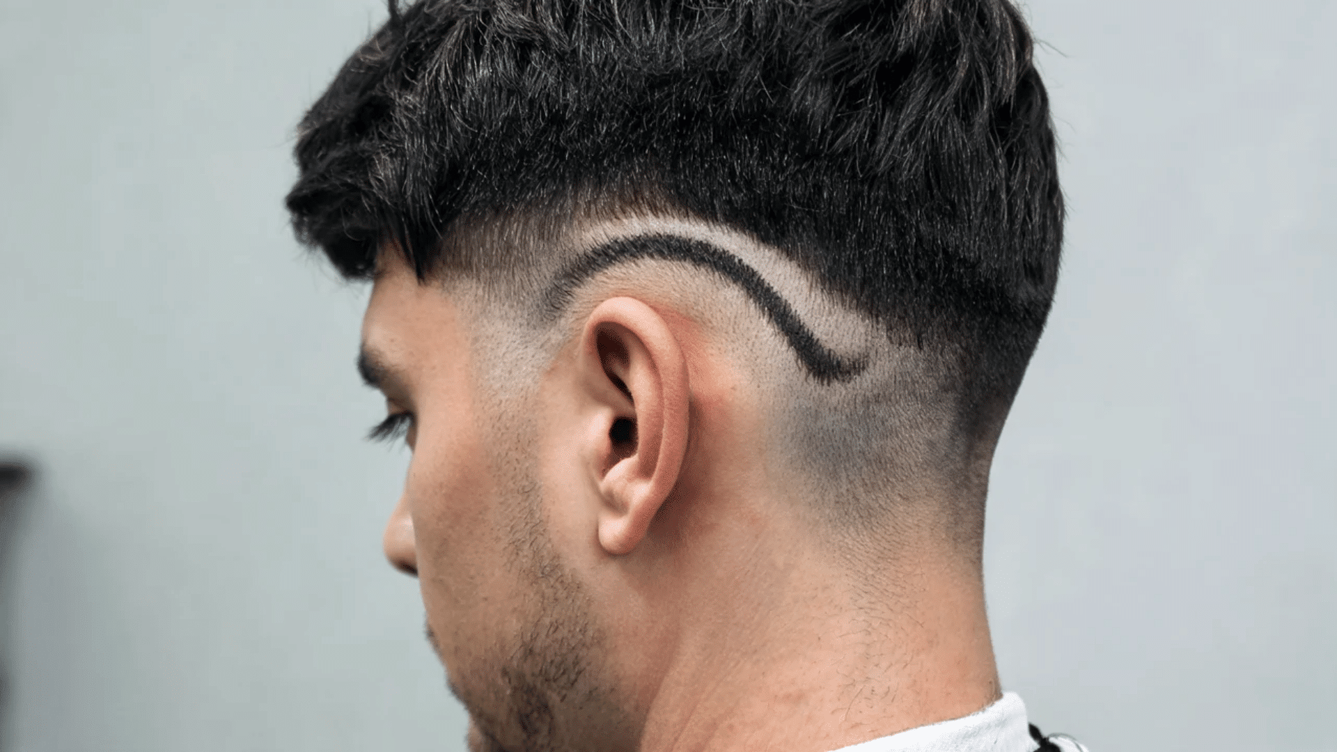 Side profile of a man showing a drop skin fade haircut with a curved fade line behind the ear and textured top.