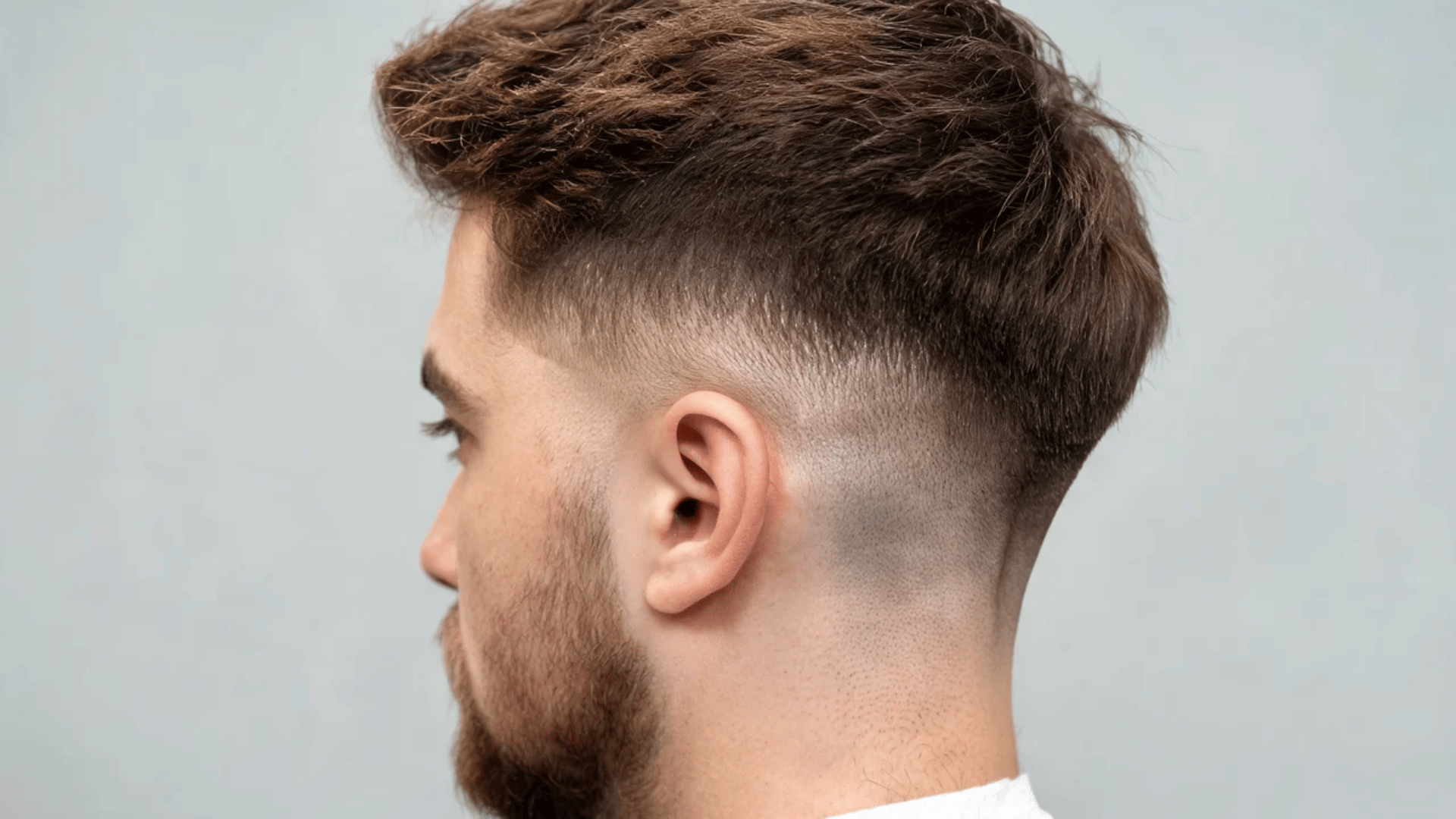 Side profile of a man showing a low skin fade haircut with a soft blend around the ears and neckline.