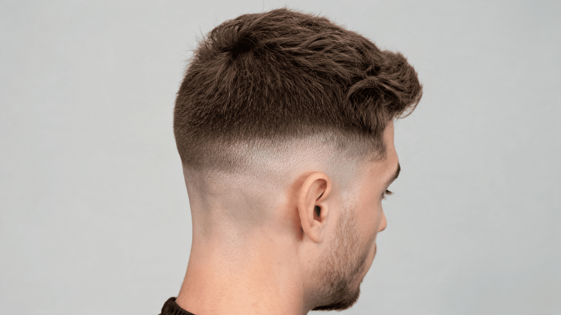 Side profile of a man showing a mid bald fade haircut with smooth blending from longer hair into skin.